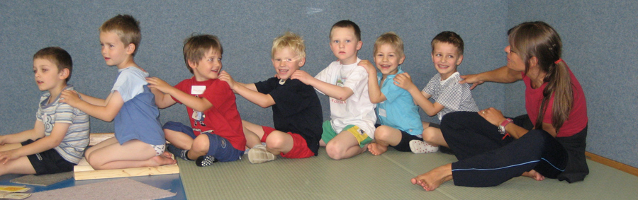 Kinder sitzen hintereinander und halten ihren Vordermann an den Schultern
